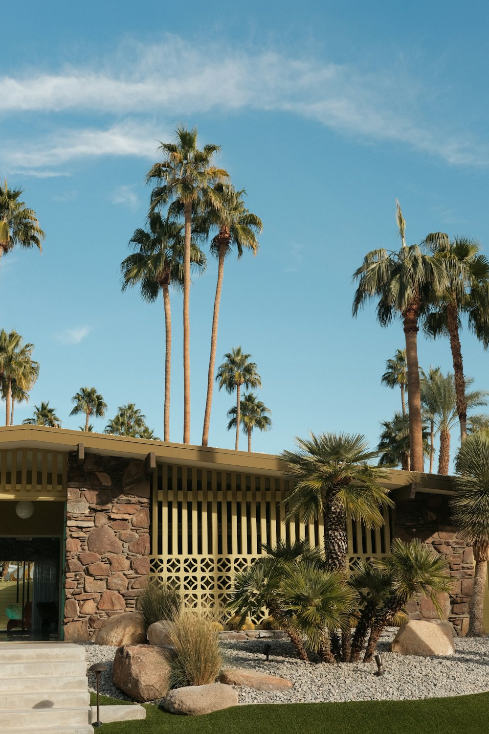 Casa moderna de mediados de siglo con muros de piedra y palmeras en Palm Springs, California